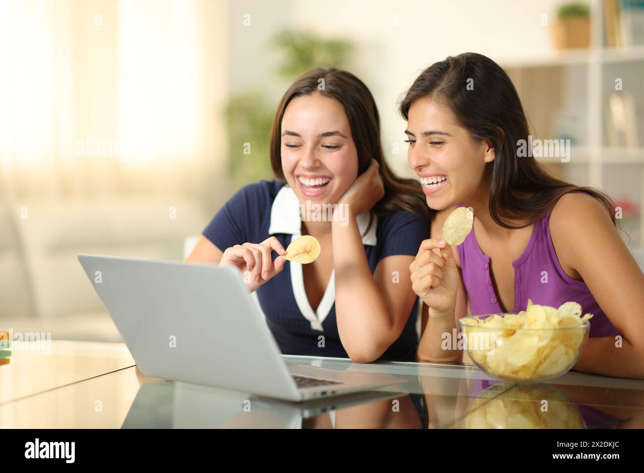 Glückliche Frauen essen Kartoffelchips und schauen sich zu Hause ein Video auf dem Laptop an Stockfoto