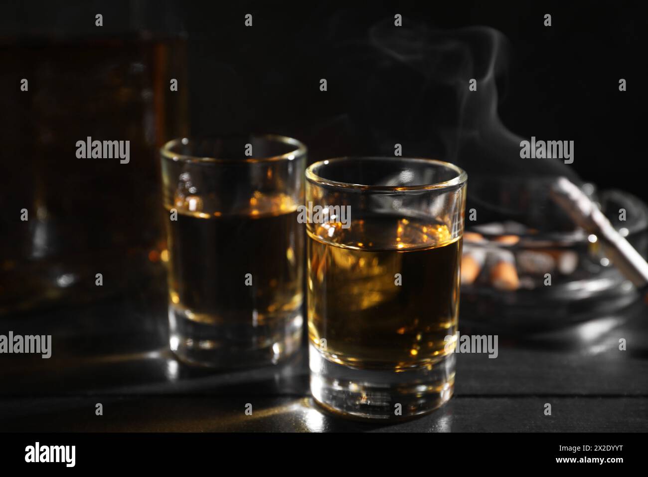 Alkoholsucht. Whiskey in Gläsern, schwelende Zigarette und Aschenbecher auf schwarzem Holztisch, Nahaufnahme Stockfoto