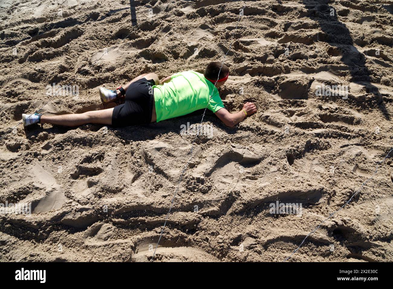 KIEW, UKRAINE - 20. APRIL 2024 - Ein Teilnehmer kriecht durch eine Schlammgrube mit Stacheldraht während des Spartan Kiew 2024 Benefizrennen auf der Insel Truchaniv, Kiew, Hauptstadt der Ukraine. Die Veranstaltung wird durchgeführt, um Geld für Drohnen für Militärangehörige und einen schwer verwundeten Soldaten des Verteidigungsnachrichtendienstes der Ukraine zu sammeln. Stockfoto