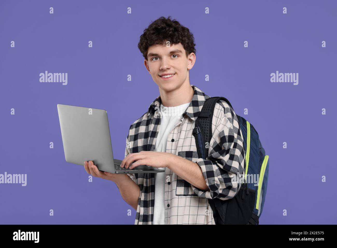 Porträt eines Schülers mit Rucksack und Laptop auf violettem Hintergrund Stockfoto