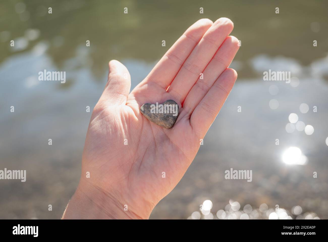 Die Frau hält einen herzförmigen Felsen in der Hand über dem Fluss Stockfoto