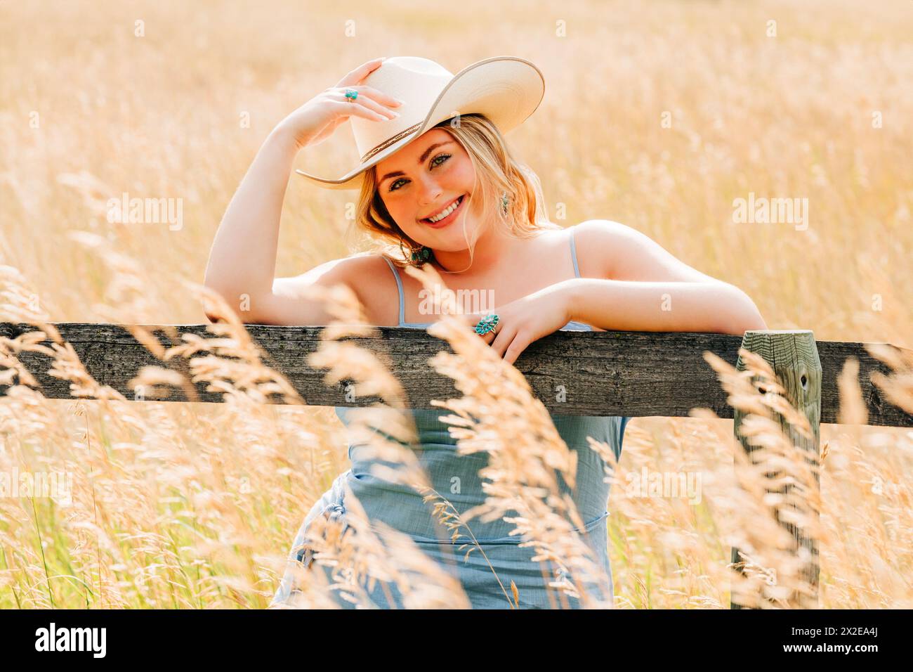 Sonniges Porträt eines Teenager-Mädchens, das mit Cowgirl-Hut am Zaun steht Stockfoto