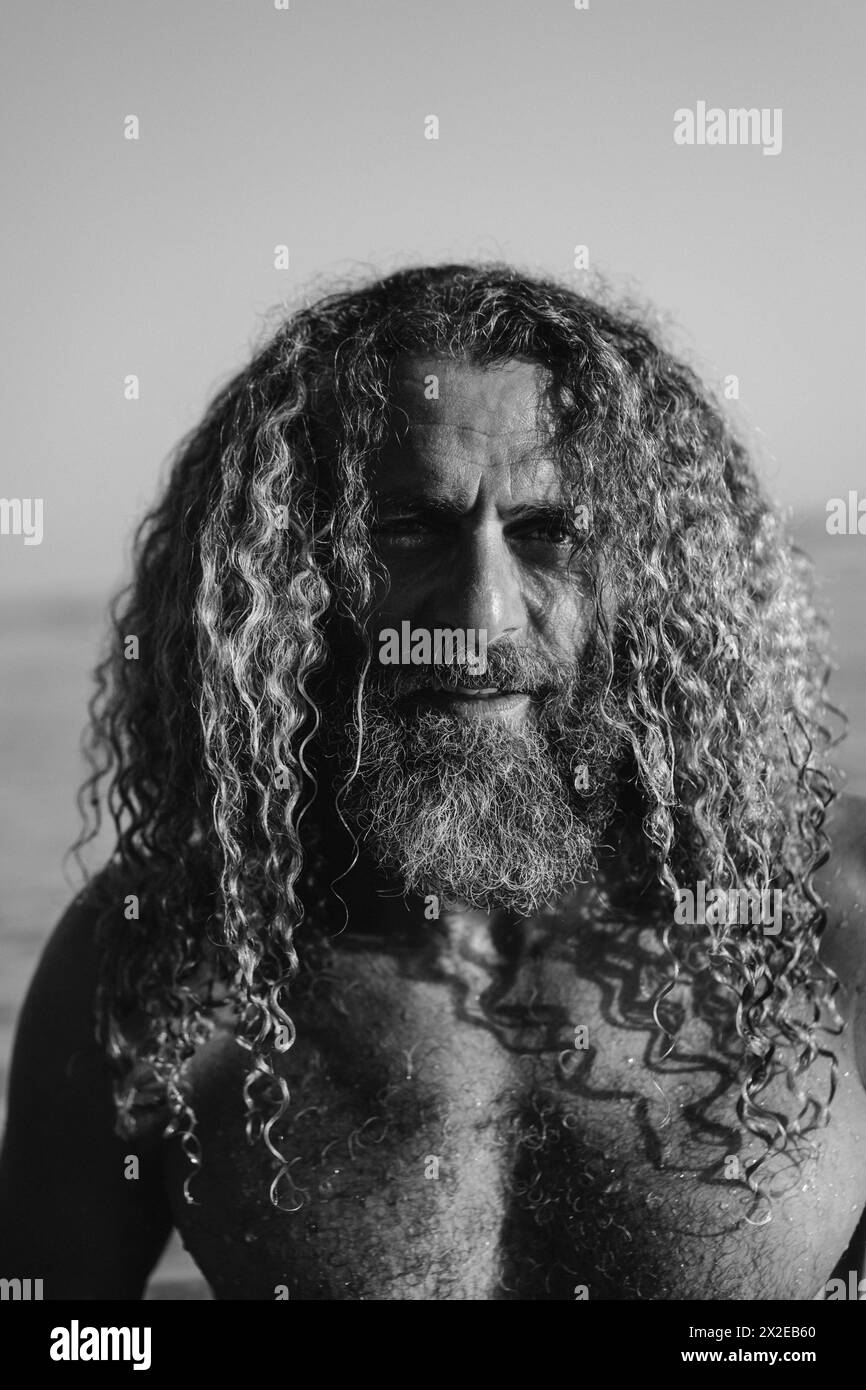 Ein Mann mit langen lockigen Haaren schwimmt im Meer. Stockfoto