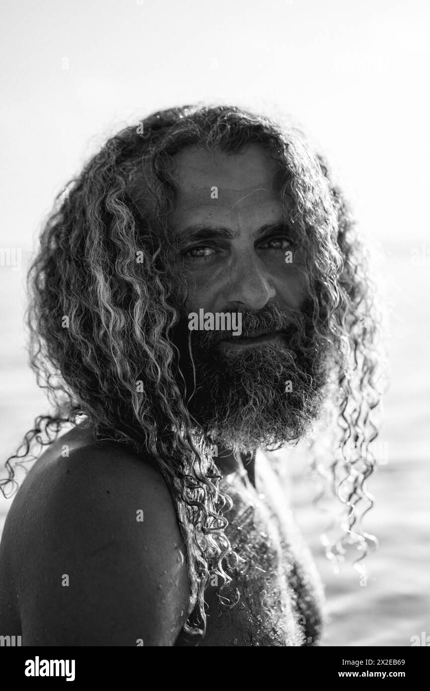Ein Mann mit langen lockigen Haaren schwimmt im Meer. Stockfoto