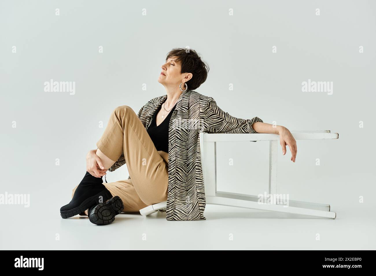 Stilvoll gekleidete Frau mittleren Alters mit kurzen Haaren sitzt auf dem Boden, die Beine sind überkreuzt und vermitteln ein Gefühl von Frieden und Selbstsicht. Stockfoto