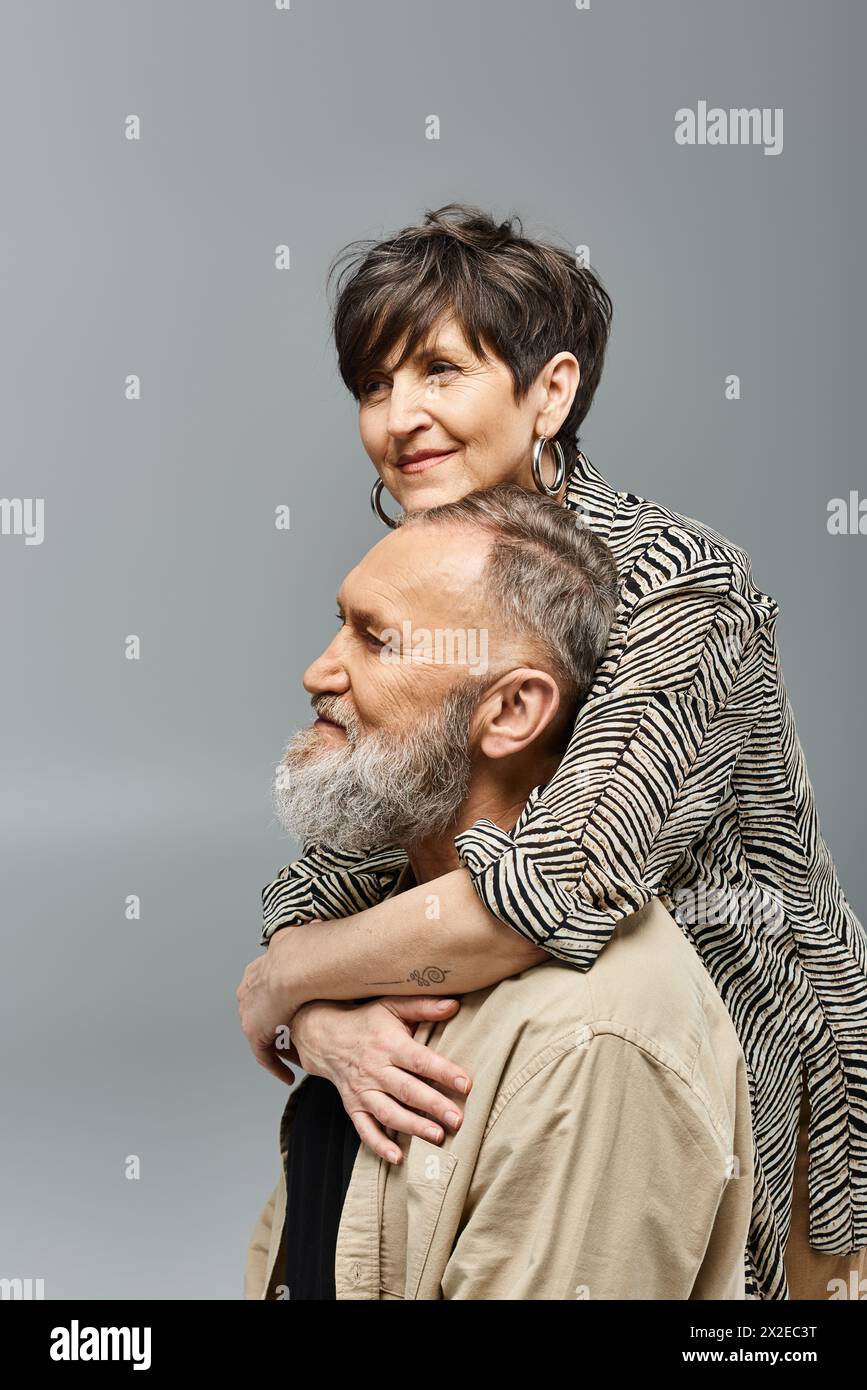 Ein Mann mittleren Alters trägt galant eine Frau auf dem Rücken in einem stilvollen Studio-Setting. Stockfoto
