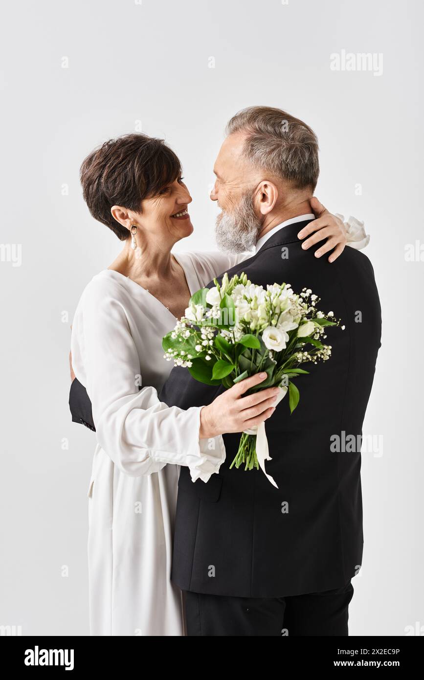 Eine Braut und ein Bräutigam mittleren Alters in Hochzeitskleidern, die sich umarmen und ihren besonderen Tag im Studio feiern. Stockfoto