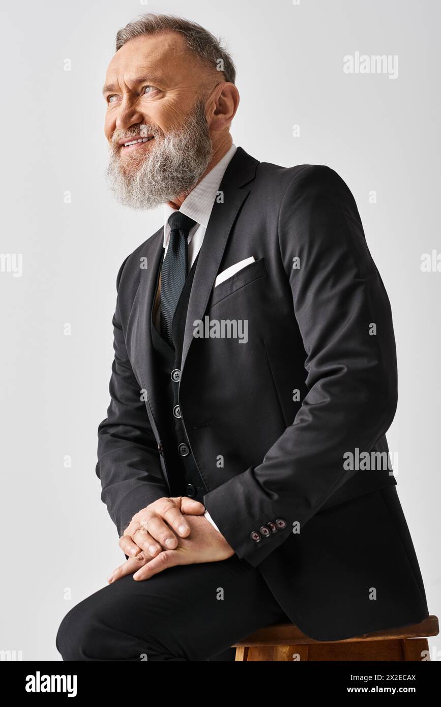 Ein Bräutigam mittleren Alters in einem eleganten Anzug sitzt an seinem Hochzeitstag in einem Studio auf einem Hocker. Stockfoto