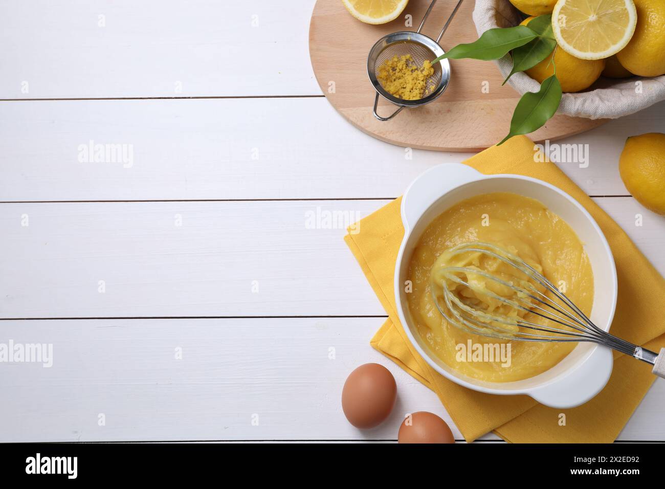 Köstlicher Zitronenquark in der Schüssel, Zutaten, Rührwerk und Sieb auf weißem Holztisch, flach gelegt. Leerzeichen für Text Stockfoto