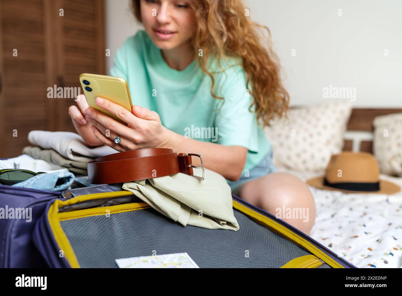 Frau, die Flugtickets kauft und das Hotel mit ihrem Handy zu Hause Bucht und Reisetasche für den Urlaub packt. Stockfoto