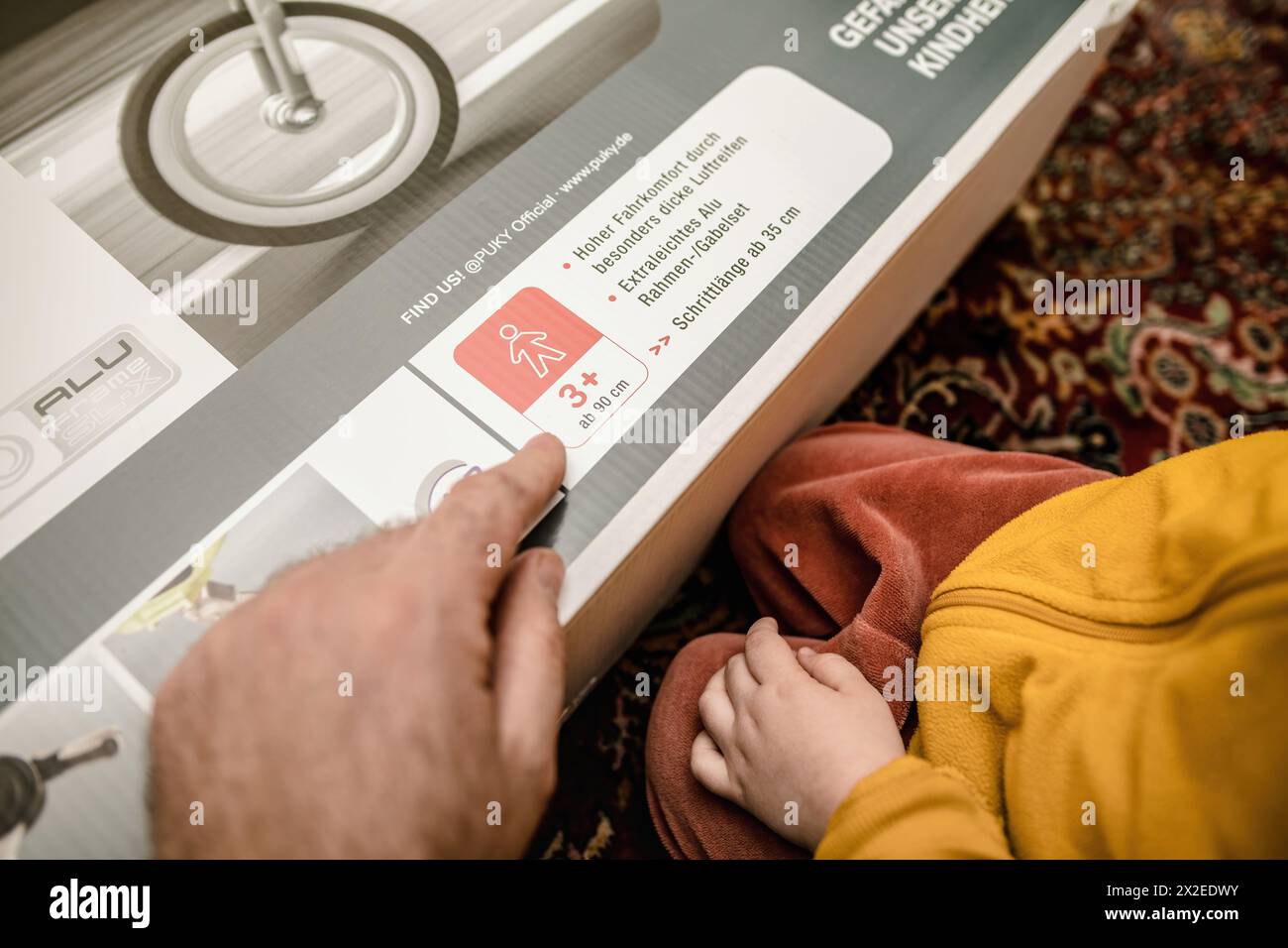 München, Deutschland - 8. April 2023: Ein Vater erklärt seinem Kleinkind, dass Lernräder für Kinder ab 3 Jahren sind, während des Ausboxens des ersten Fahrrads des Kindes. Stockfoto