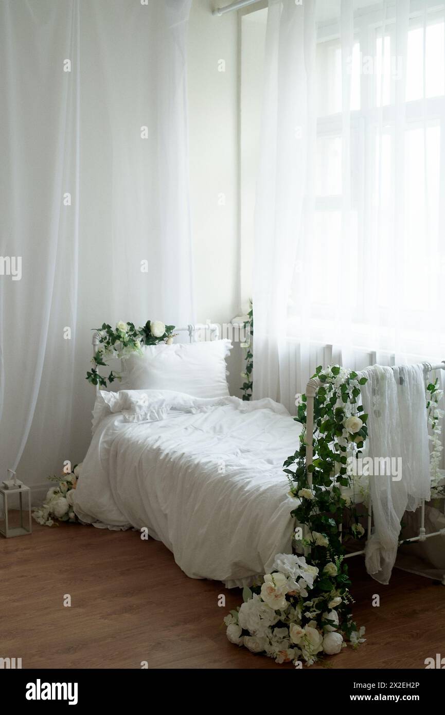 Rustikales Bett mit Blumen und weißer Baumwollbettwäsche. Metallrahmen. Stockfoto
