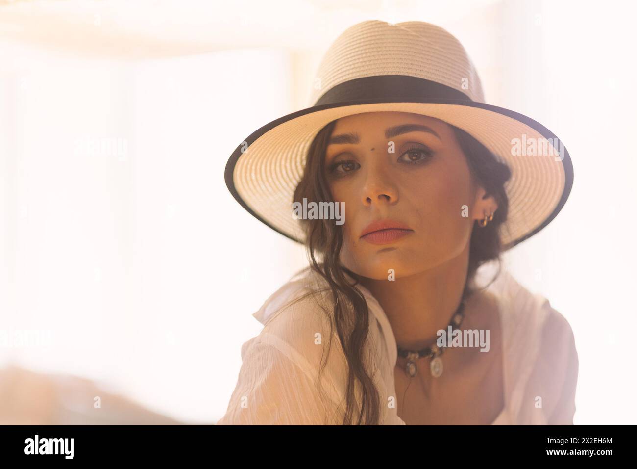 Elegante, modische Frau in sommerweißem Kleid, Strohhut, posiert in stilvollem Boho-Interieur. Kopieren, leerer Platz für Text Stockfoto