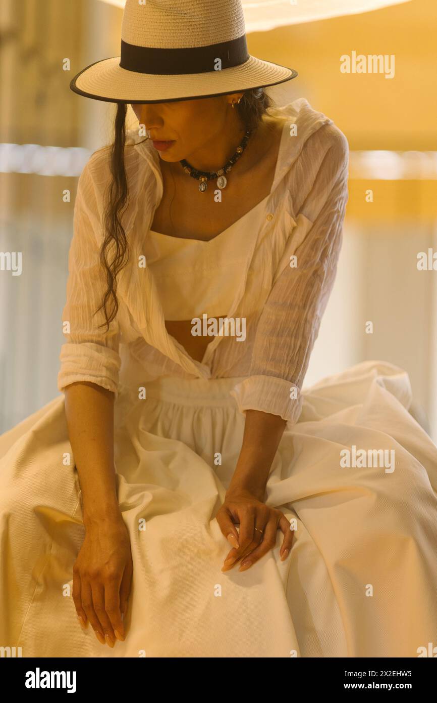 Elegante, modische Frau in sommerweißem Kleid, Strohhut, posiert in stilvollem Boho-Interieur. Kopieren, leerer Platz für Text Stockfoto