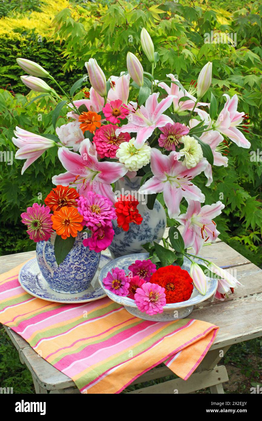 Botanik, Lilien und Zinnien in blau-weißen Krügen und Schüsseln auf einem Tisch im Freien, EXTRA-RIGHTS-CLEARANCE-INFO-NOT-AVAILABLE Stockfoto