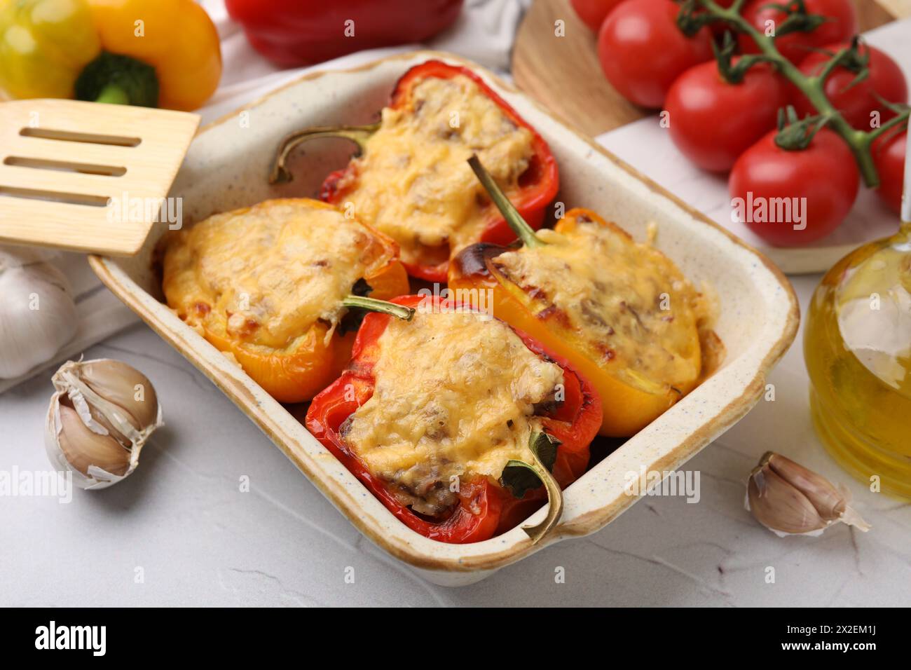 Köstliche gefüllte Paprika in Backform, Spachtel und Zutaten auf weißem, strukturiertem Tisch, Nahaufnahme Stockfoto