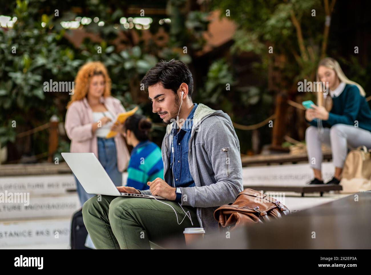 Porträt eines männlichen Studenten, der mit Laptop auf dem Campus sitzt. Stockfoto