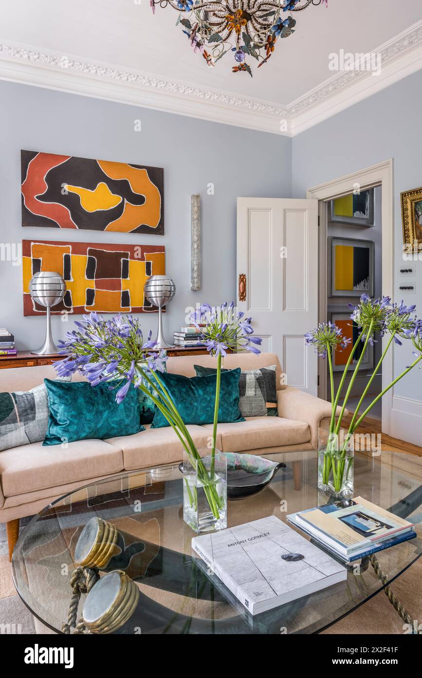 Moderne Kunstwerke über beigefarbenem Sofa mit Schnittblumen auf Couchtisch im georgianischen Stadthaus. Paultons Square, Chelsea, London, Großbritannien. Stockfoto