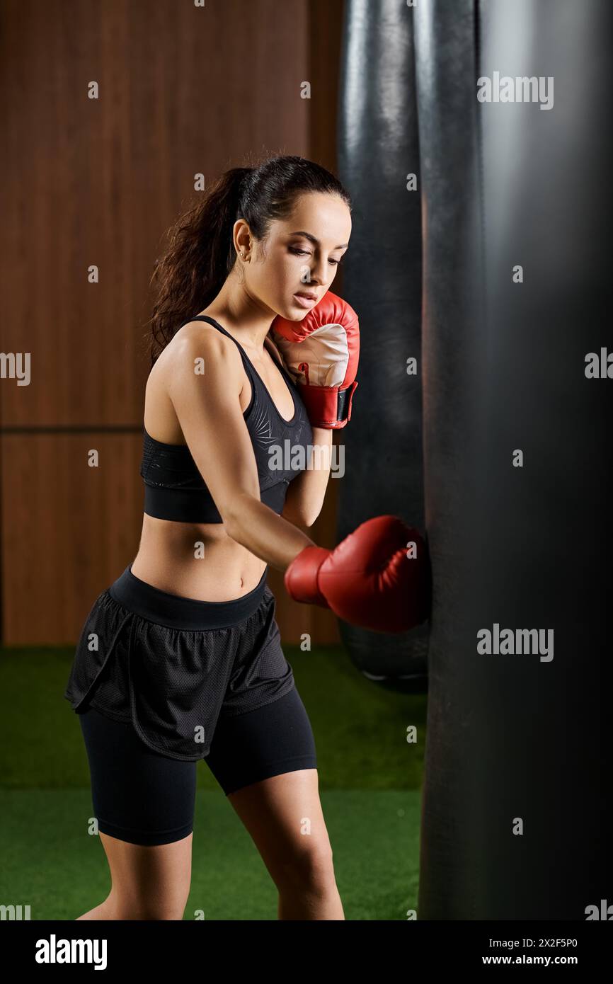 Eine brünette Sportlerin in schwarzem Oberteil und Shorts konzentriert sich auf das Boxen im Fitnessstudio mit Kraft und Entschlossenheit. Stockfoto