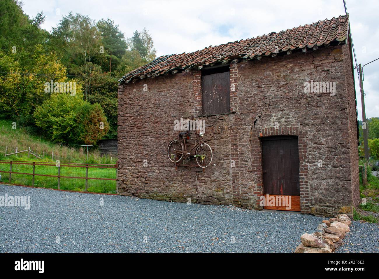 Ein altes rostiges Fahrrad hängt an der Seite einer Scheune, die in den Ardennen, Belgien, fotografiert wurde Stockfoto