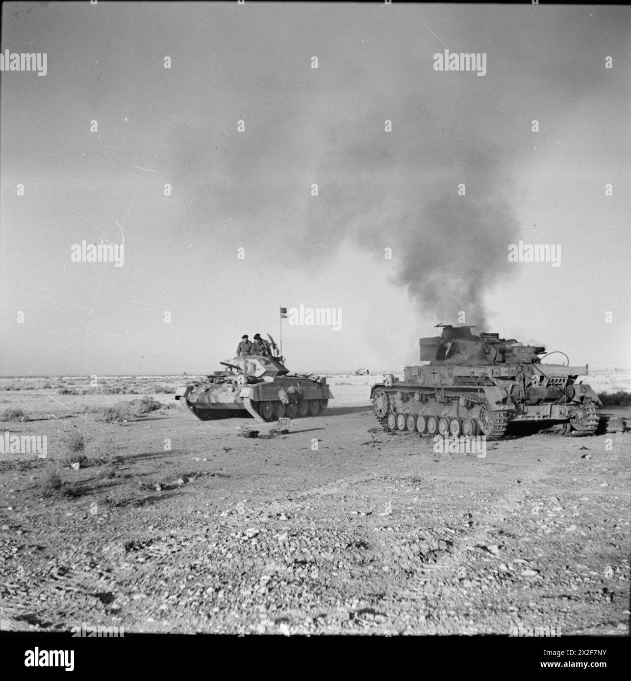 Ein britischer Kreuzfahrerpanzer fährt am 27. November 1941 in Nordafrika an einem zerstörten deutschen Panzer IV vorbei, was die Panzereinsätze der Westwüstenkampagne veranschaulicht. Stockfoto