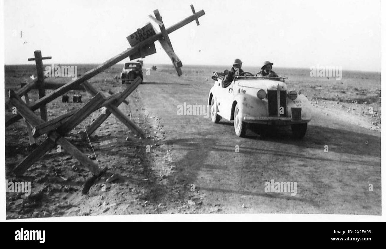 Fotos in Bardia zeigen eine zuvor gesperrte Straße, die wieder eröffnet wurde, mit einem kleinen Wagen der britischen Armee, der durch eine verdrängte Barriere fährt. Stockfoto