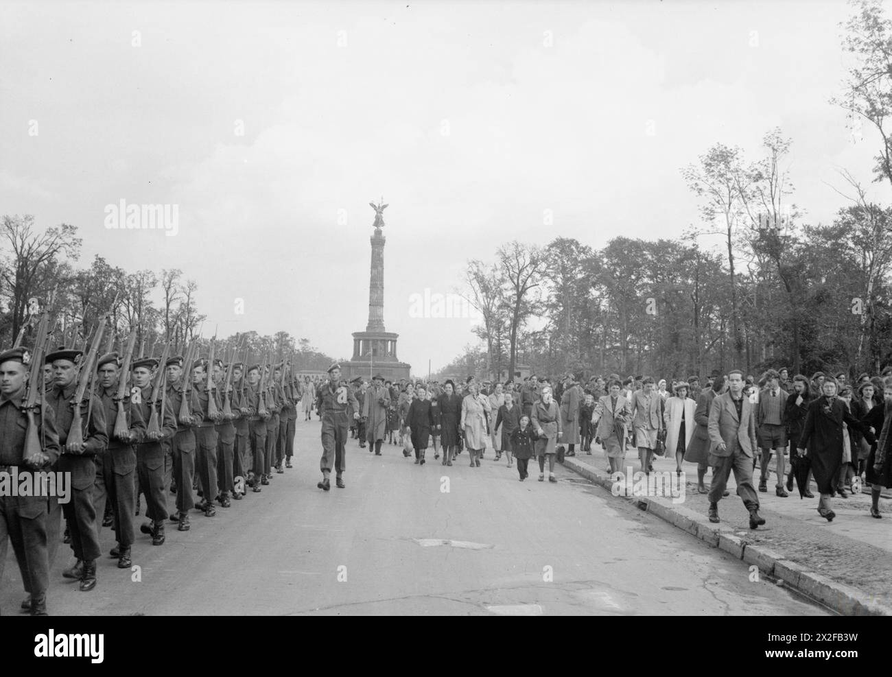 Britische Truppen marschieren während der Zeremonie „Brechen the Flag“ zum Beginn der alliierten Besatzung im Jahr 1945 die Charlottenburger Chaussee in Berlin hinunter, wobei deutsche Zivilisten beobachtet wurden. Stockfoto
