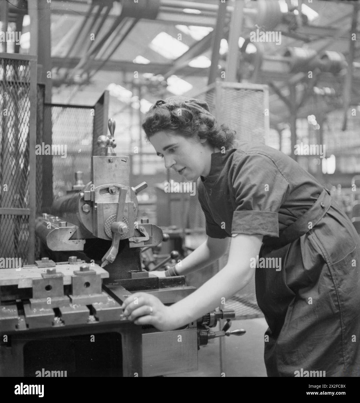 KRIEGSARBEIT IN DER FRAUENFABRIK IM SLOUGH TRAINING CENTRE, ENGLAND, Großbritannien, 1941 - Ruby May arbeitet an einer Maschine, wahrscheinlich einer mechanischen Säge, im Slough Training Centre Stockfoto