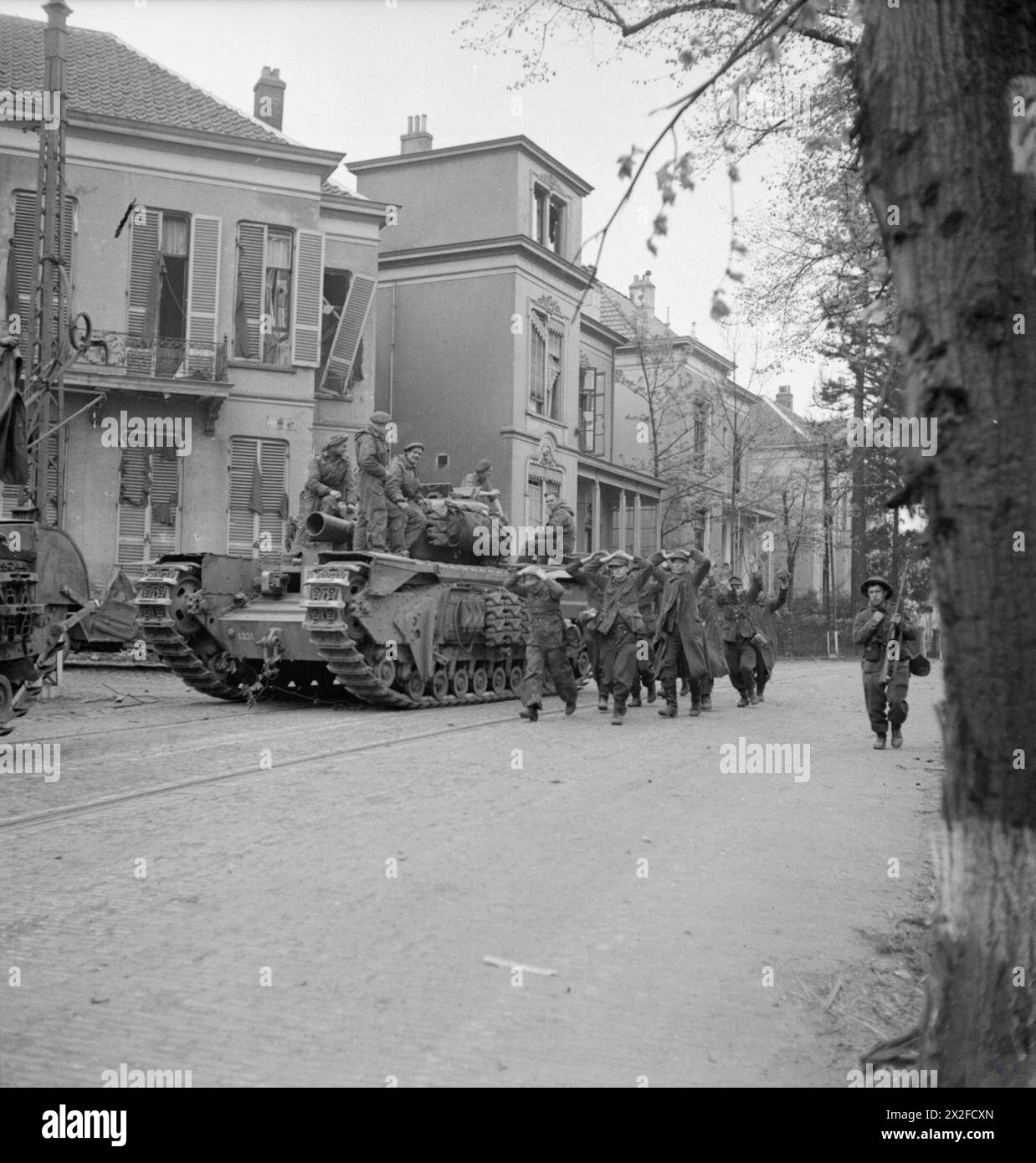 Deutsche Kriegsgefangene marschieren am 14. April 1945 im Rahmen der Operationen der British Army und Royal Engineers in Nordwesteuropa an einem Churchill AVRE-Panzer vorbei. Stockfoto