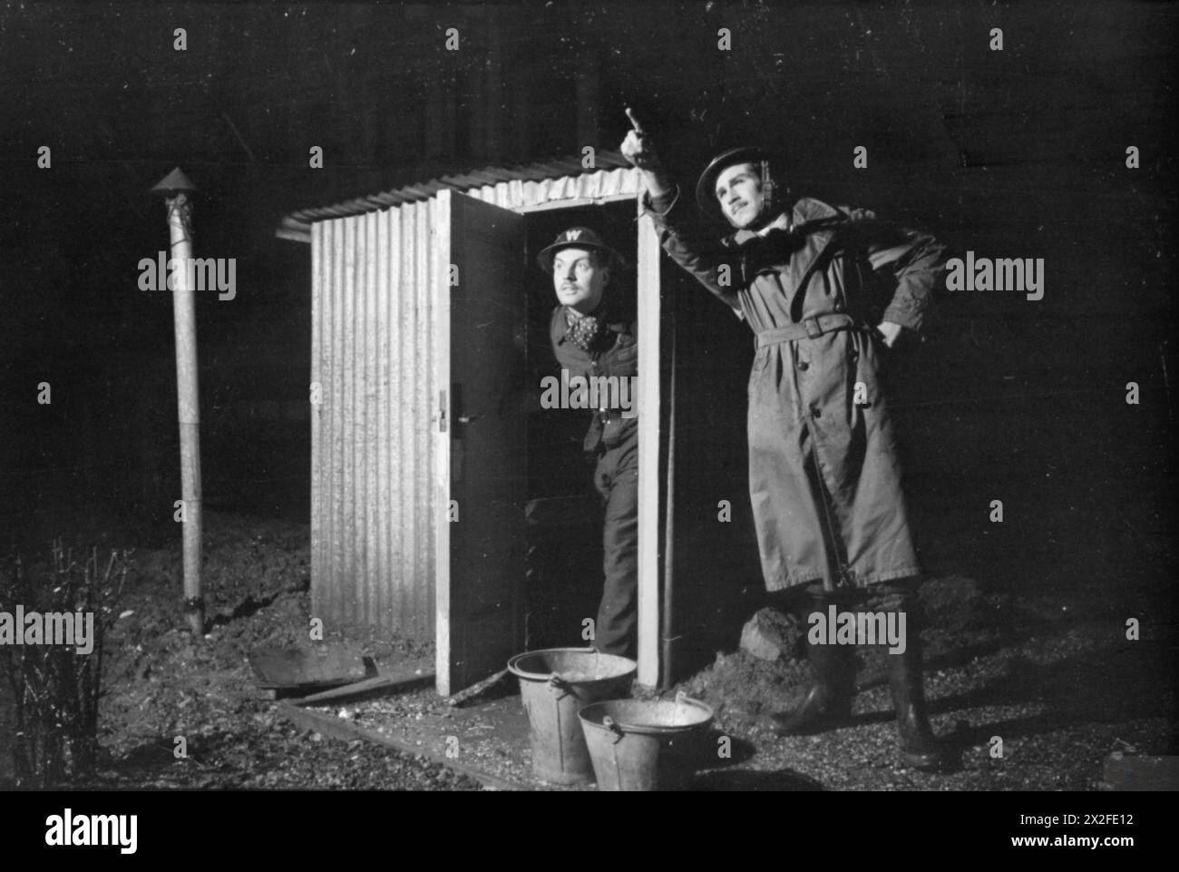 LONDON AFS: MÄNNER DER HILFSFEUERWEHR IN LONDON, C 1940 - zwei Air RAID Vorkehrungen Wardens stehen an ihrem ARP-Posten. Ein Wächter befindet sich direkt in der Wellblechhütte (die über einem Betonschacht gebaut ist), während der andere Wächter in die Skyline zeigt, nachdem er ein Feuer entdeckt hat Stockfoto