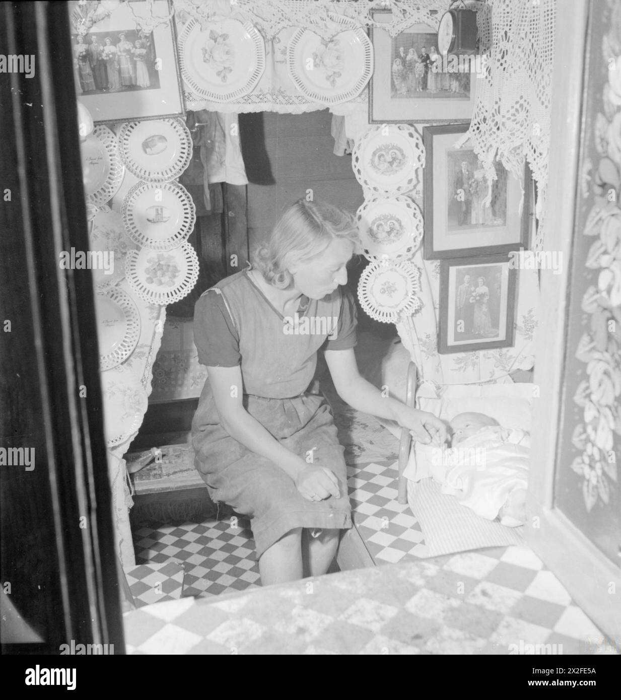 Eine Mutter lässt ihr Baby 1944 in der Kabine eines Kanalbootes in Großbritannien nieder. Die Kabine ist mit dekorativen Platten, Familienfotos und Spitze ausgestattet, die die typischen Innenräume des Kanalbootes während des Transports während des Krieges widerspiegeln. Stockfoto