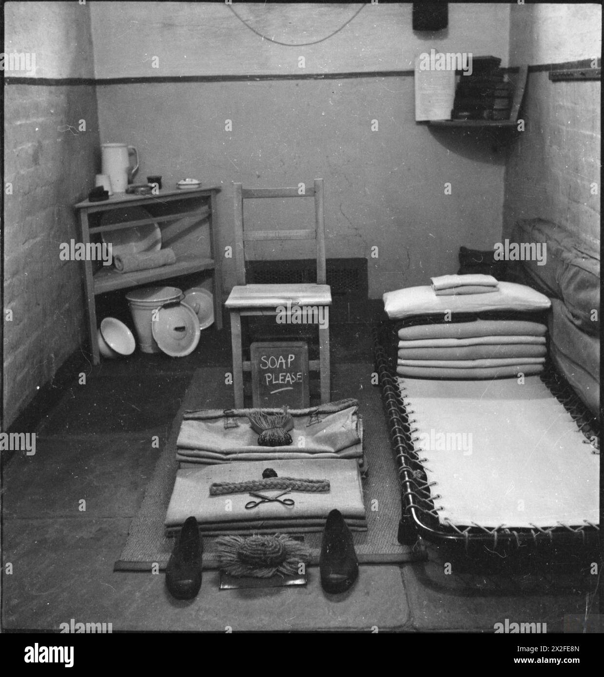 WAKEFIELD-AUSBILDUNGSGEFÄNGNIS UND -LAGER: ALLTAG IN Einem BRITISCHEN GEFÄNGNIS, WAKEFIELD, YORKSHIRE, ENGLAND, 1944 - Ein Blick auf das Zimmer eines Häftlings im Wakefield-Gefängnis. Deutlich sichtbar sind das Bett, ein Stuhl, mehrere kleine Regale und ein Schaufel. Der Rest der Sachen des Häftlings, wie ein Paar Schuhe und ein Kamm, wurde ordentlich aufgestellt, bereit zur Inspektion. Auf einer kleinen Tafel sind die Worte „Seife bitte“ gemalt. Stockfoto