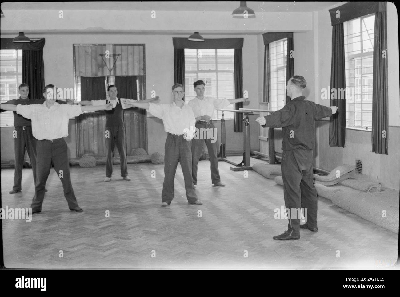 REHABILITATION BRITISCHER SOLDATEN AUS DER NORMANDIE: DIE ARBEIT DES ROBERT JONES AND DAME AGNES JAGDKRANKENHAUSES, OSWESTRY, SHROPSHIRE, ENGLAND, VEREINIGTES KÖNIGREICH, 1944 - während der späteren Behandlungsphasen im Robert Jones and Dame Agnes Hunt Orthopaedic Hospital, Oswestry, erhalten verletzte Soldaten eine Ausbildung von einem Armeeausbilder. Hier stehen die Männer in Reihen, die Arme sind zu beiden Seiten gestreckt. Einer der Patienten scheint nur einen Arm zu haben Stockfoto