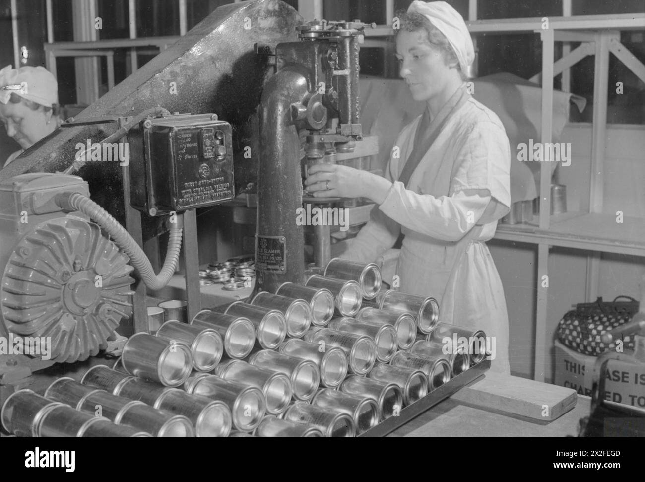 Ein ERSATZ FÜR CHININ: DIE HERSTELLUNG VON MEPACRIN IN Einer FABRIK IN DER NÄHE VON LONDON, ENGLAND, Großbritannien, 1945 - Frau Florence Brewer verwendet eine Maschine, um Dosen von Mepacrin-Tabletten in einer pharmazeutischen Fabrik in der Nähe von London mit einer Maschine zu versehen. Die Dosen sind voll mit den Anti-Malaria-Pillen und wurden in Baumwollwolle verpackt, wobei auch gedruckte Anweisungen hinzugefügt wurden, bevor die Dosen versiegelt werden. Laut der Originalüberschrift dient Mrs. Brewers Bruder in Indien bei der RAF: "Sie hofft, dass er eine Dosis Chinin braucht, bekommt er eine der Pillen, die sie einpackt." Stockfoto