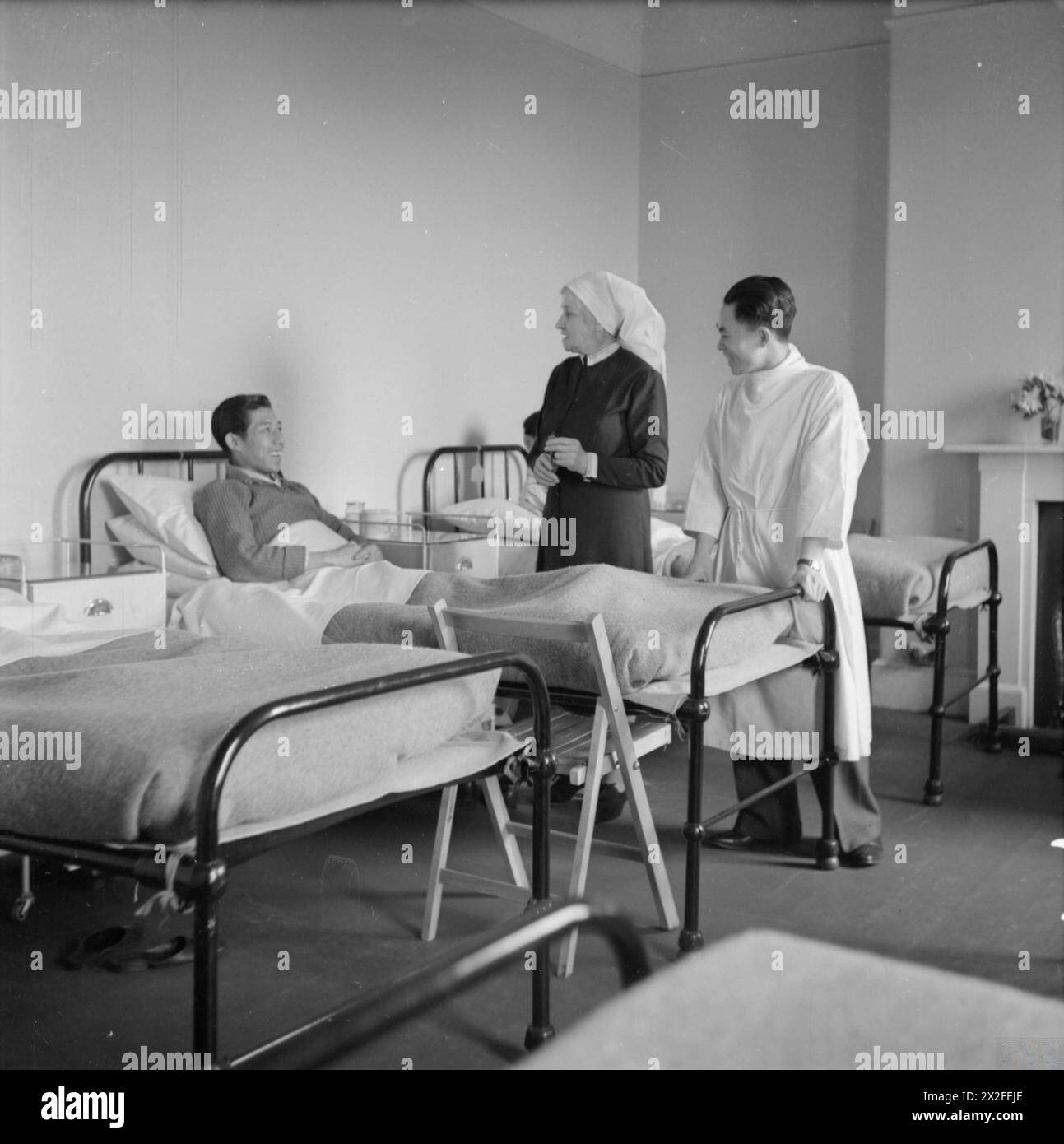 CHINESISCHES ERHOLUNGSHEIM: ERHOLUNG FÜR SEELEUTE IN LIVERPOOL, ENGLAND, 1943 – Matron Miss S Beattie und Dresser Chow Ding Yee sprechen mit einem Patienten im Bett in einer Station des chinesischen Erholungshauses in Liverpool. Nach der Originalüberschrift arbeitete Matron 20 Jahre lang in China mit der Chinesischen Missionarsgesellschaft und diente 4 Jahre lang in Frankreich, während des Ersten Weltkriegs. Die Kommode war ein Steward auf einem chinesischen Schiff, hofft aber, sich als Arzt zu qualifizieren Stockfoto