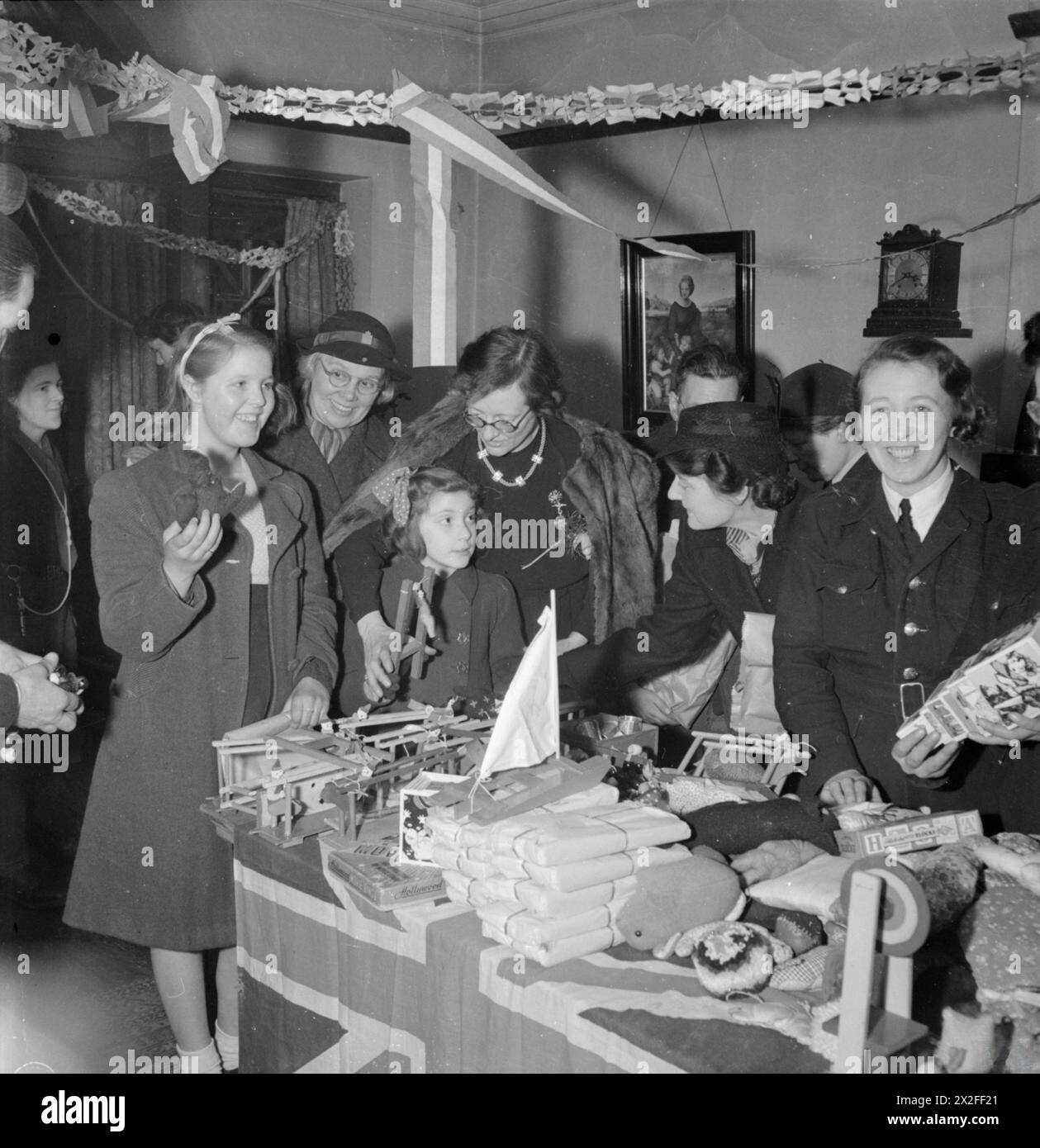 Miss Constance Holland unterstützt Norma Terry und Doreen Jones bei der Auswahl von Weihnachtsgeschenken von American Aid im Canning Town Settlement in London im Dezember 1944. Der Raum ist mit Papierschlangen und einem WVS-Mitglied ausgestattet. Stockfoto
