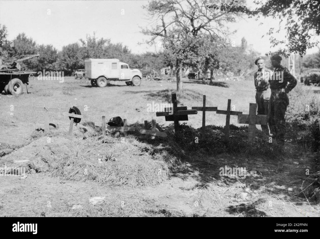 DIE POLNISCHE ARMEE IM NORMANDIE-FELDZUG 1944 – Truppen der 1. Polnischen Panzerdivision (möglicherweise 24. Panzerregiment, 10. Panzerbrigade) pflegen nach der Schlacht von Falaise Gap im August 1944 Gräber ihrer gefallenen Kameraden. Der Offizier auf der rechten Seite hat den Rang eines Hauptmanns. Gefangengenommene deutsche 10,5 cm leFH 18M Leichtfeldhaubitze und Sturmgeschütz III (StuG III) Panzerzerstörer sind im Obstgarten im Hintergrund zu sehen polnische Armee, polnische Streitkräfte im Westen, 1. Panzerdivision, polnische Streitkräfte im Westen, 1. Panzerdivision, 10. Panzerbrigade, Polnisch Stockfoto