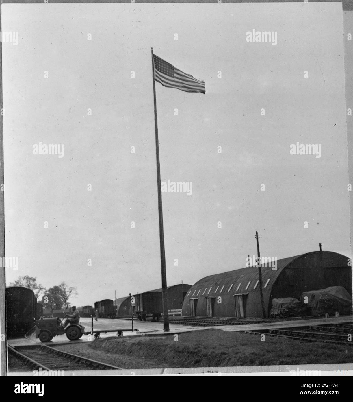 Die amerikanische Flagge fliegt über Romney-Hütten in einem britischen Lager, das als Lebensmittelgeschäft für die amerikanische Armee dient. Der Privatmann Robert L Starling, ehemals ziviler Lkw-Fahrer, betreibt einen LKW, der Vorräte liefert. Das Lager bietet logistische Unterstützung und Lagerung für amerikanische Truppen in Großbritannien. Stockfoto