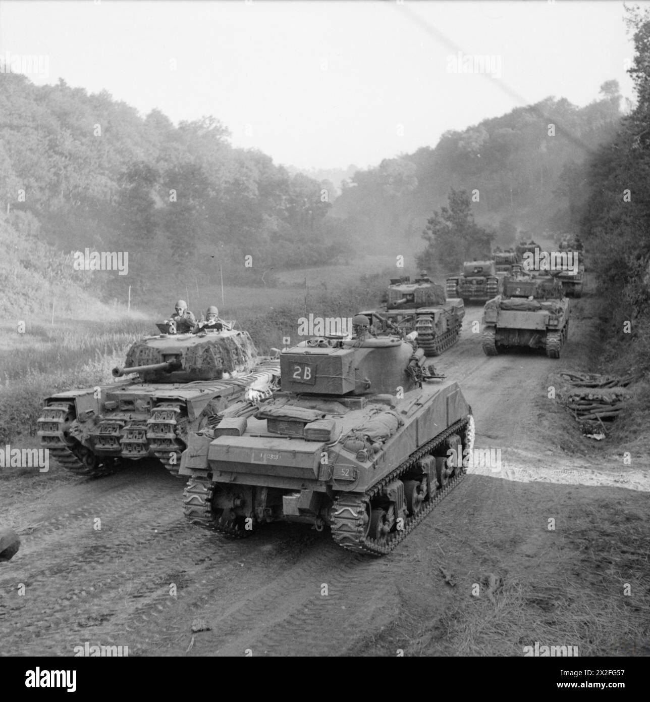 DIE BRITISCHE ARMEE IM NORMANDIE-FELDZUG 1944: Sherman-Panzer, die nach Süden fahren, passieren eine Kolonne von Churchills der 4. Grenadier Guards, 6. Guards Panzerbrigade, während sie am 4. August 1944 in Richtung Vassy vorrücken. Forschungen deuten darauf hin, dass dieses Foto außerhalb des Dorfes Cathéolles La Bas in Souleuvre en Bocage in der Normandie, Frankreich, aufgenommen wurde. Informationen von Veteranen und veröffentlichten Arbeiten zeigen, dass dieses Foto außerhalb des Dorfes Cathéolles La Bas, Souleuvre en Bocage, Normandie, Frankreich, auf der heutigen Straße D577 und nicht auf der Hauptstraße Vassy (heute D512) gemacht wurde. Stockfoto