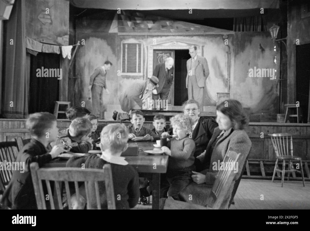 Die Old Vic Traveling Theatre Company errichtete 1941 die Bühne in der Settlement Hall in Trealaw, Wales. Frauen und Kinder essen eine Mahlzeit im Vordergrund, da der Saal auch als Futterstelle dient. Stockfoto