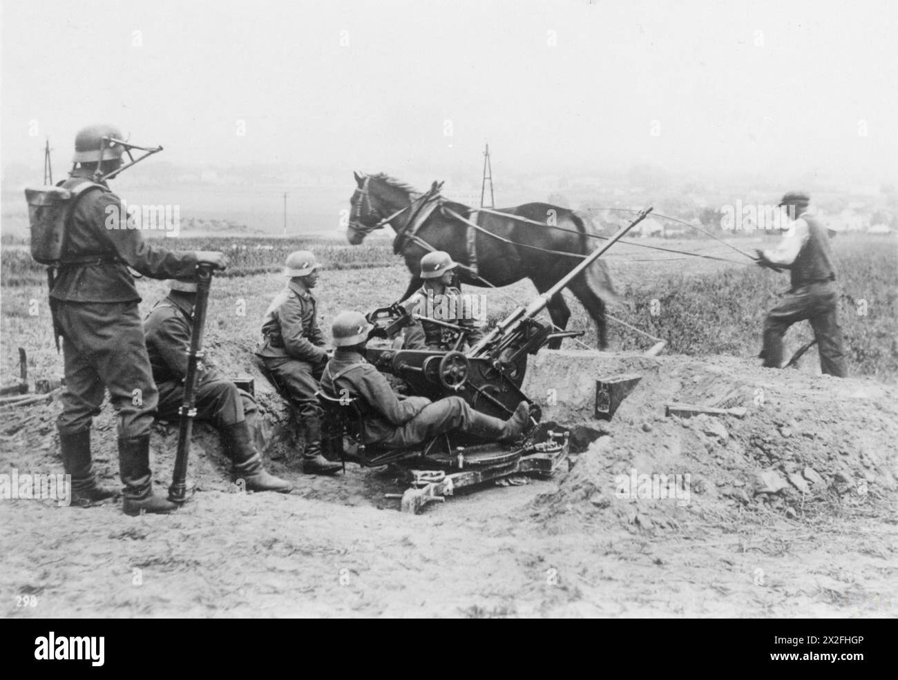 Deutsche Soldaten betreiben im Oktober 1939 während des Scheinkriegs an der französischen Grenze eine 2 cm große Flak 30 leichte Flugabwehrkanone. Ein Bauer pflügt sein Feld in der Nähe mit einem Pferd, während ein Soldat links einen auf einem tragenden Rahmen montierten Entfernungsmesser hält. Stockfoto