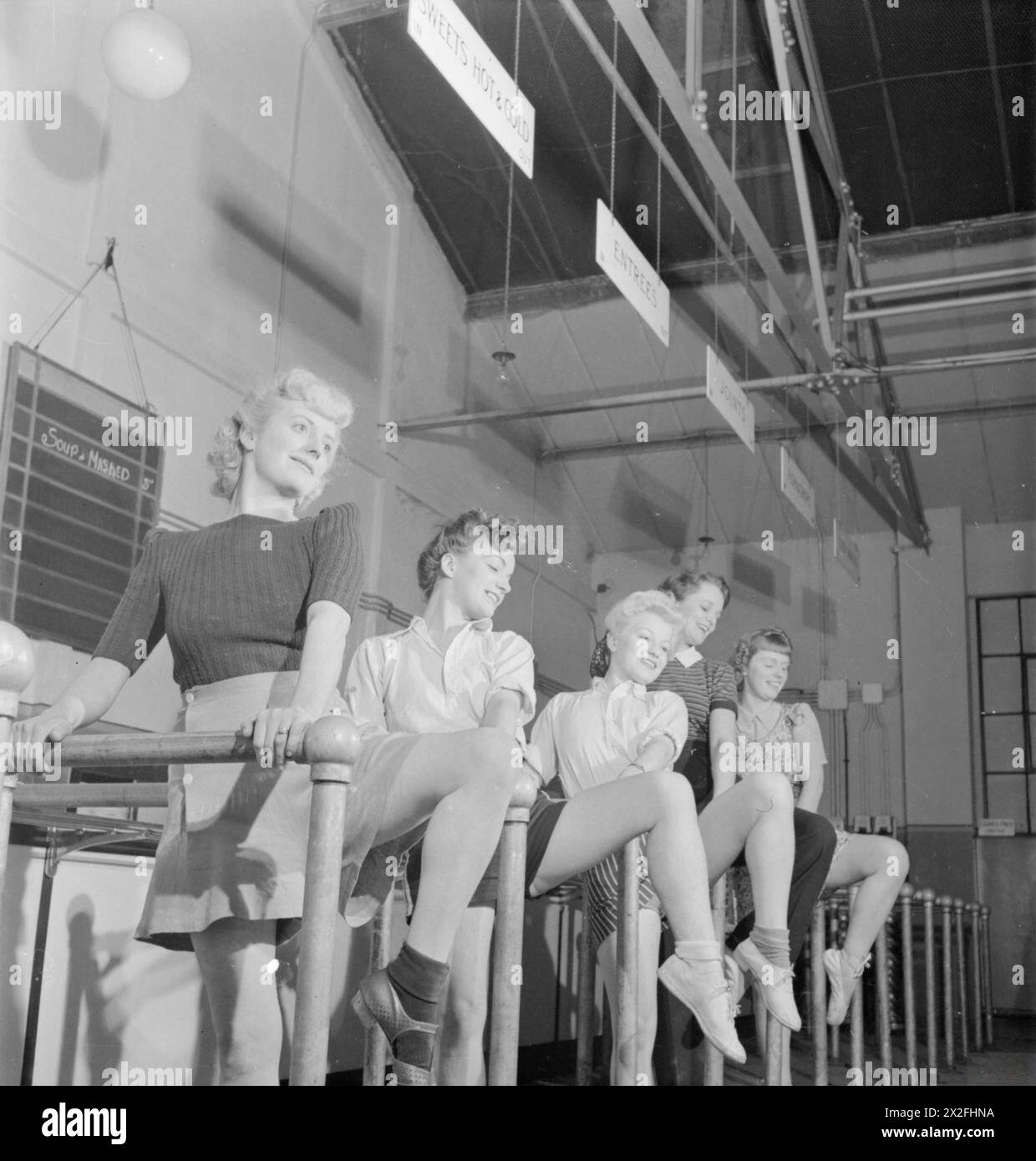 FACTORY BALLET: WARTIME FACTORY ENTERTAINMENT, 1942 – weibliche Fabrikarbeiter, darunter Florence Simpson, Winifred Bennett und ihre Schwester Dolly, üben am Ende ihrer Schicht einige Ballettzüge in der Kantine der Flugzeugfabrik, in der sie arbeiten, irgendwo in Großbritannien. Sie benutzen die Bars, die die Warteschlangen der Gäste trennen, als Barren Stockfoto