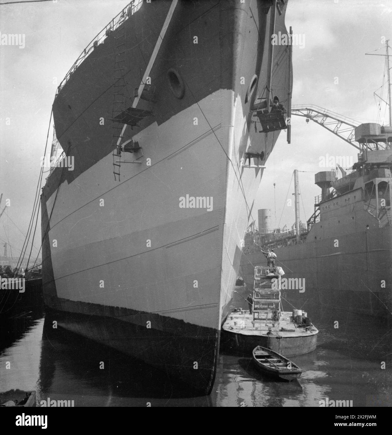 Arbeiter malten 1944 das Äußere eines neuen Frachtschiffes auf einer Glasgower Werft, wobei sie lange Pinsel und Gerüste über dem Deck eines Lastkahns benutzten, um schwierige Bereiche während des Schiffsbaus zu erreichen. Stockfoto