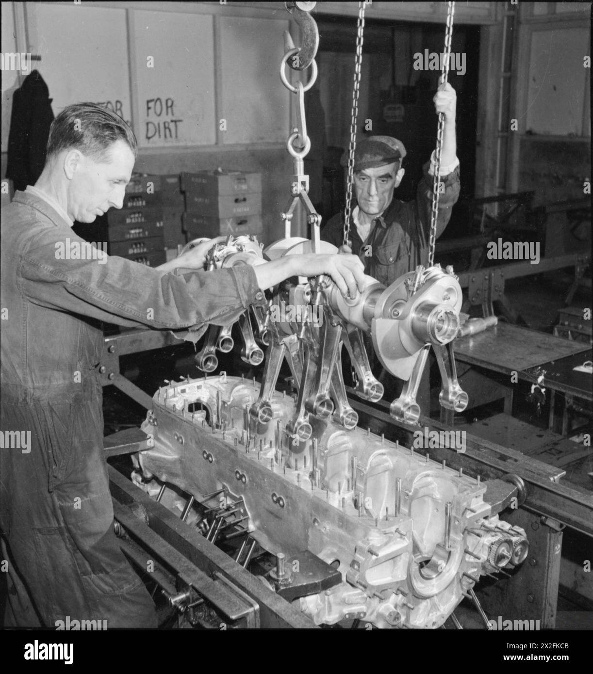 Ein MERLIN WIRD HERGESTELLT: DIE PRODUKTION VON MERLIN-MOTOREN IN Einer WALZEN ROYCE-FABRIK, 1942 – zwei Arbeiter in dieser Flugzeugmotorfabrik senken die Kurbelwellenbaugruppe sanft in das Kurbelgehäuse ab Stockfoto