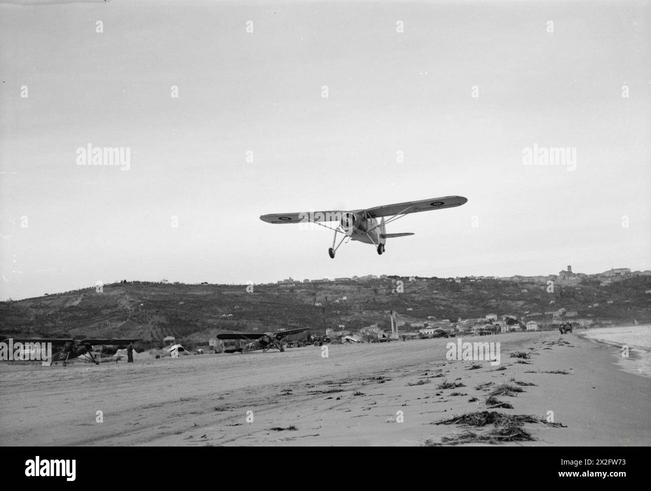 KÖNIGLICHE LUFTWAFFE: ITALIEN, BALKAN UND SÜDOSTEUROPA, 1942-1945. - Ein Fairchild Argus der Desert Air Force Communication Flight startet vom Strand in Vasto, Italien, der von Dezember 1943 bis März 1944 als Landeplatz für das Hauptquartier der Desert Air Force diente. Links vom Strand parkt der Fiesler Storch, der vom Air Officer Commanding DAF, Air Vice-Marshal H Broadhurst, mit Vultee-Stinson Vigilants, ebenfalls vom DAF Communications Flight Royal Air Force, Air Force, Western Desert, geflogen wird Stockfoto