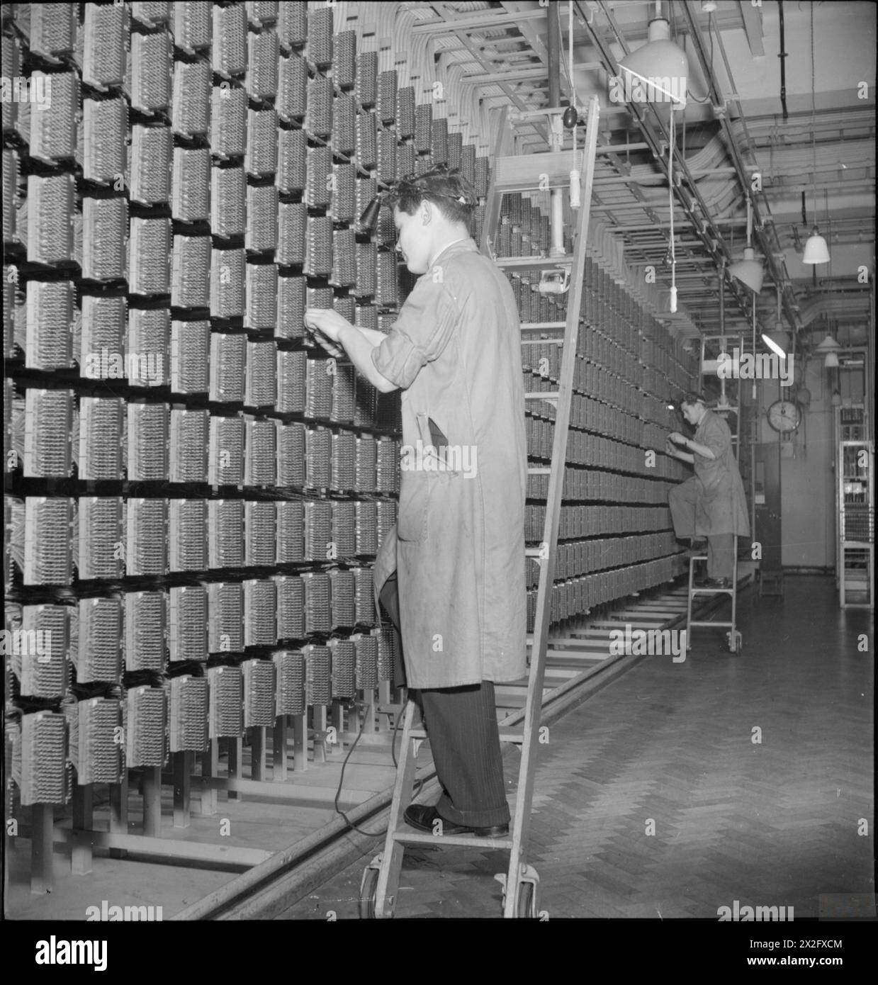 Die Ingenieure arbeiten 1945 am Zwischenverteilerrahmen an einer Londoner Telefonzentrale, verbinden Kabel vom Hauptrahmen und prüfen die Geräte auf Überlastungen, um Fehler zu lokalisieren. Stockfoto