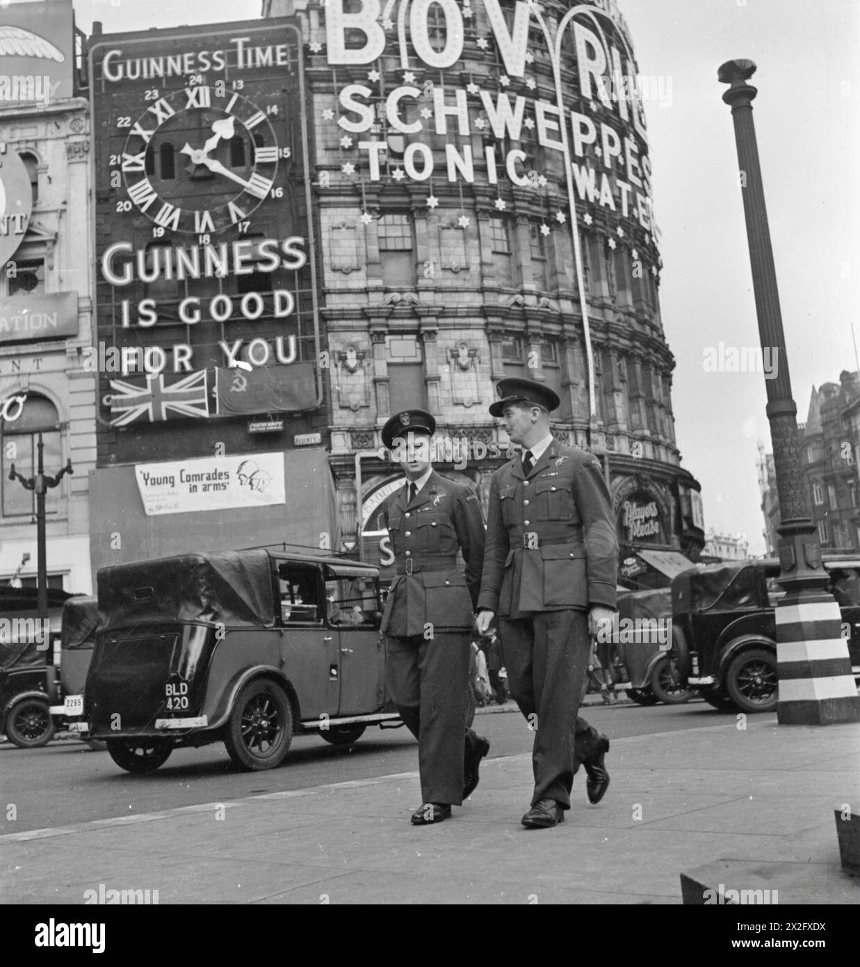 DIE POLNISCHE LUFTWAFFE IN GROSSBRITANNIEN, 1940-1947 - Flugleutnant Zbigniew Duńczewski und Fliegender Offizier Zdzisław Hirsz von der polnischen Bombergeschwader Nr. 304, die einen Spaziergang rund um den Piccadilly Circus machen, während sie auf Abreise sind, 1942. Hinter ihnen stehen Leuchtanzeigen für Bovril und Schweppes Tonic Water, und eine Uhr enthält die Worte „Guinness Zeit“ und „Guinness ist gut für dich“. Auch die Fahrzeuge bahnen sich ihren Weg durch den „Zirkus“ hinter den beiden Männern polnische Luftwaffe, polnische Luftwaffe, Bombergeschwader des Landes Schlesien 304, Duńczewski, Zbigniew, Hirsz, Zdzisław W. Stockfoto