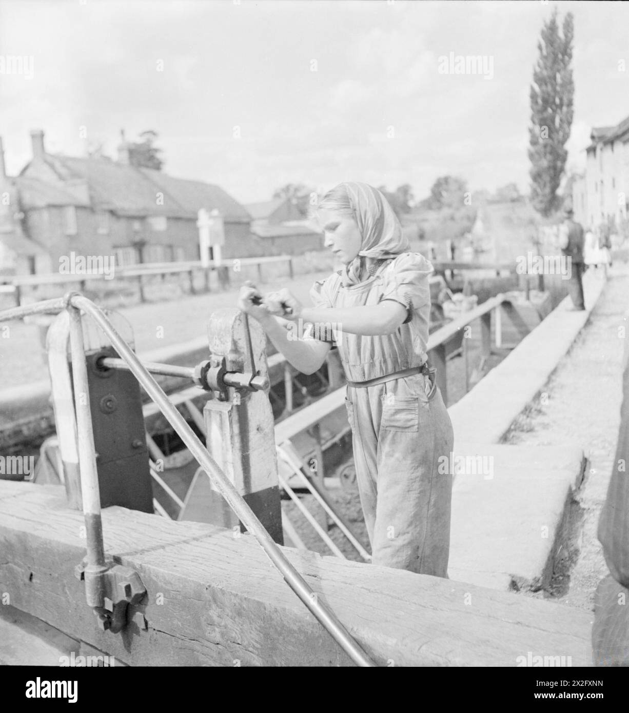 BRITISH CANALS IN WARTIME: TRANSPORT IN BRITAIN, 1944 - Eine junge Tochter eines Kanalschiffers dreht den Griff eines Schleppers irgendwo entlang des Grand Union Canal. Sie zieht die Paddel hoch, damit das Wasser von der oberen Ebene die Schleuse füllen und die Boote anheben kann. Der Originaltitel besagt, dass jedes Mal, wenn ein Paar Boote hoch oder runter fährt, eine Wasserschleuse verwendet wird (5,600 Gals). Wasser wird gespart, indem Boote abwechselnd in entgegengesetzte Richtungen hindurchfahren. Wenn ein Paar Boote gerade hochgefahren ist, ist die Schleuse voll für ein Paar, das absteigt. Stockfoto