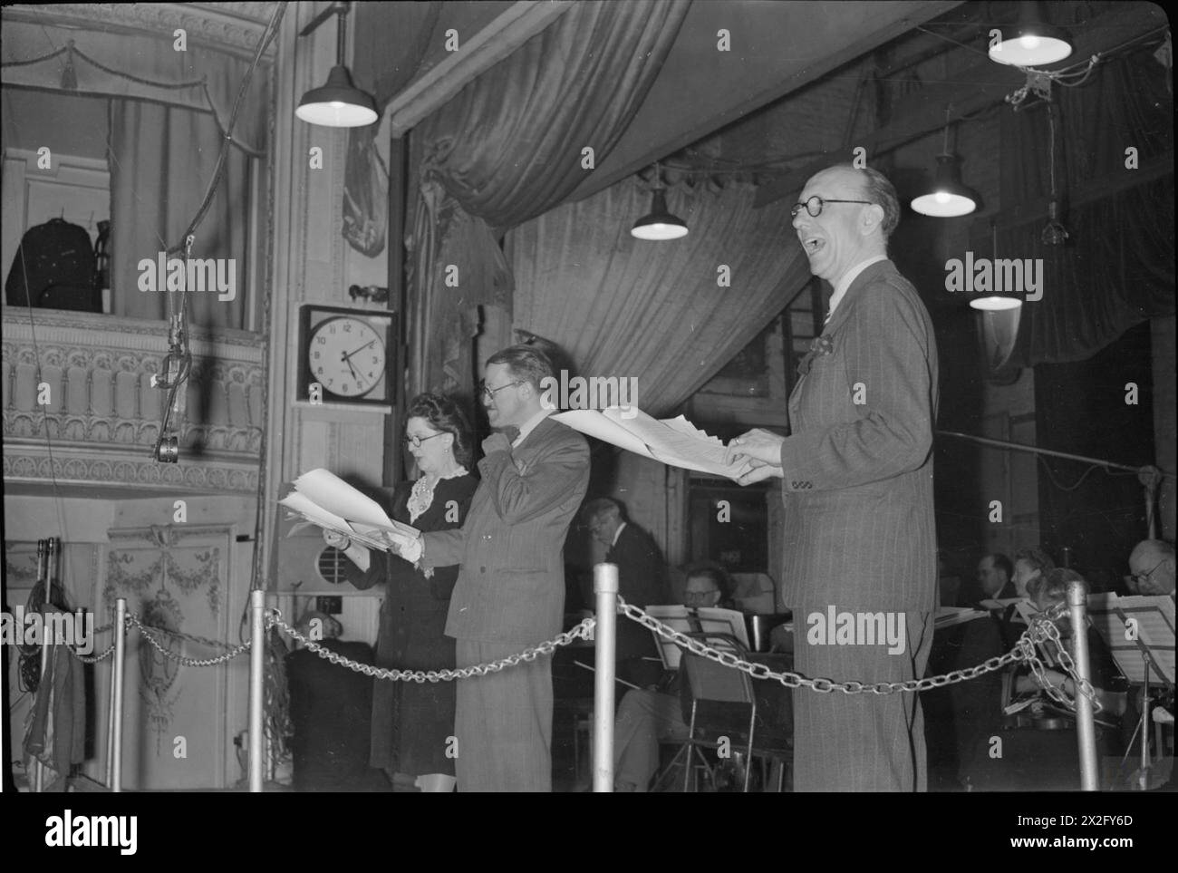 Während einer Aufnahme von IT's That man Again in London im Jahr 1945 interagiert der Dirigent Charlie Shadwell mit den Künstlern Tommy Handley und Dorothy Summers, mit dem BBC Variety Orchestra auf der Bühne. Stockfoto