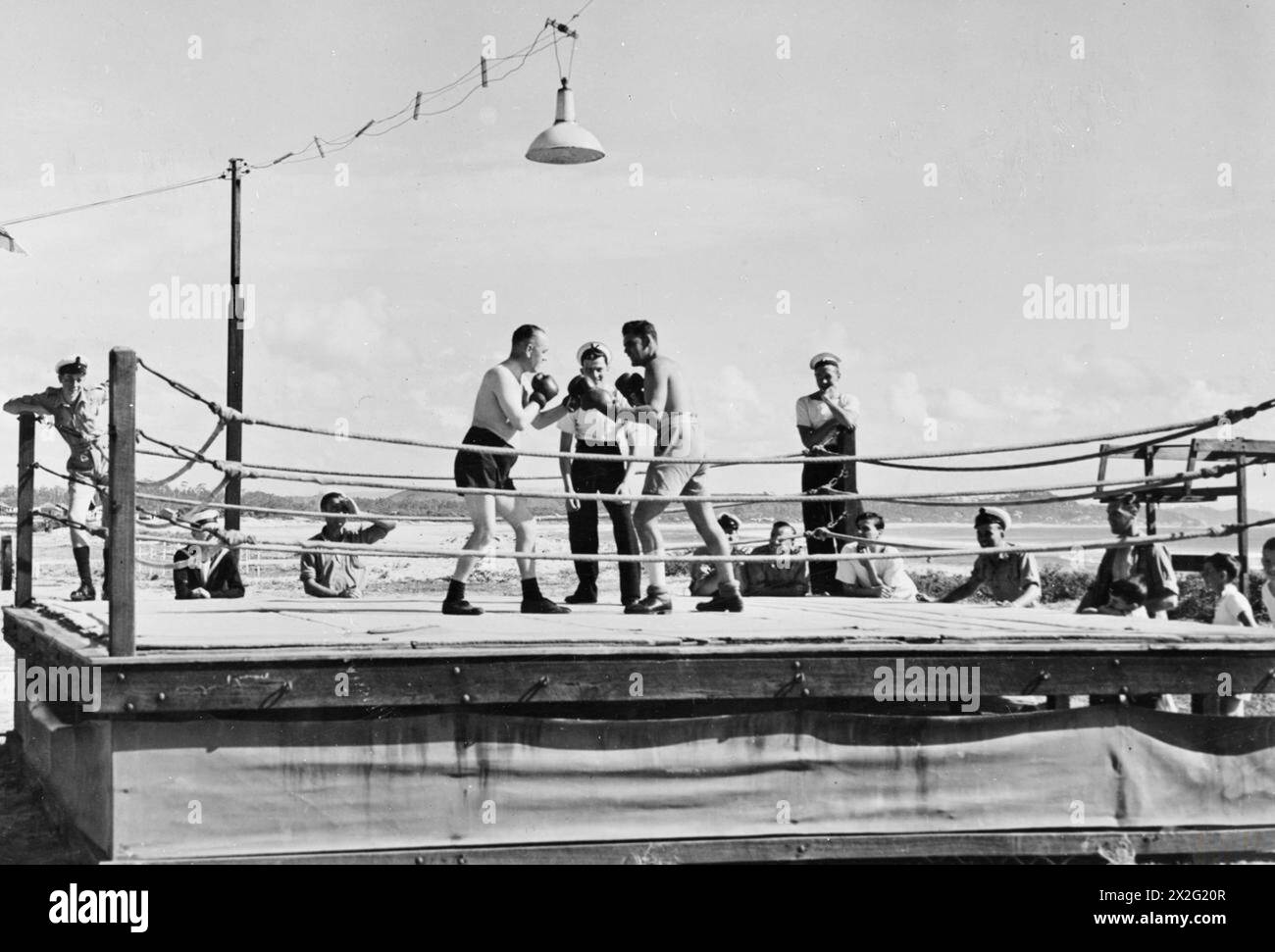 DIE BRITISCHE MARINE IM URLAUB. AUGUST 1945, MARINELASTLAGER IN COOLANGATTA, QUEENSLAND, AUSTRALIEN. DIE MARINESTÜTZPUNKTE KÖNNEN EINEN WOHLVERDIENTEN URLAUB IN COOLANGATTA GENIESSEN, EINEM KOSTENLOSEN FERIENLAGER MIT ALLEN ANNEHMLICHKEITEN EINER ERSTKLASSIGEN ZIVILEN ORGANISATION. ES WIRD AUCH ALS ERHOLUNGSZENTRUM VON PATIENTEN DES ROYAL MARINEKRANKENHAUSES IN BRISBANE GENUTZT. - Ein freundlicher Kampf im Open Air Boxring in Coolangatta Stockfoto